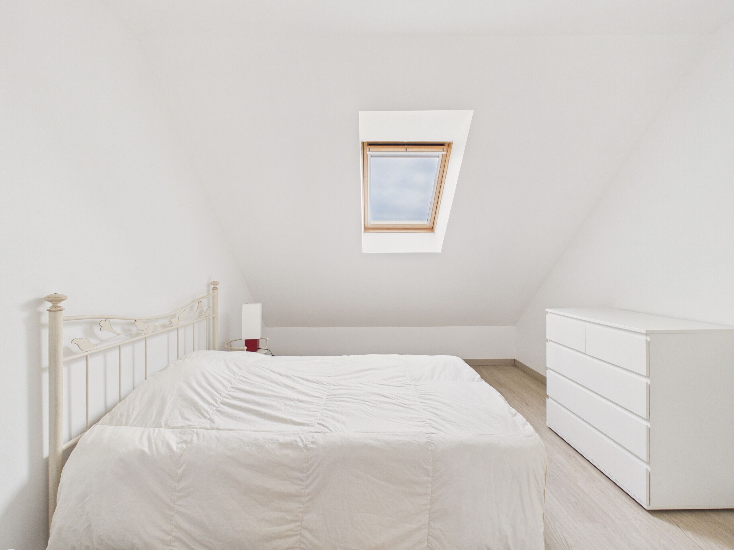 A bedroom with a bed, a dresser, a nightstand, and a skylight.