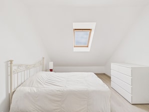 Une chambre à coucher comprenant un lit, une commode, une table de chevet et un puits de lumière.