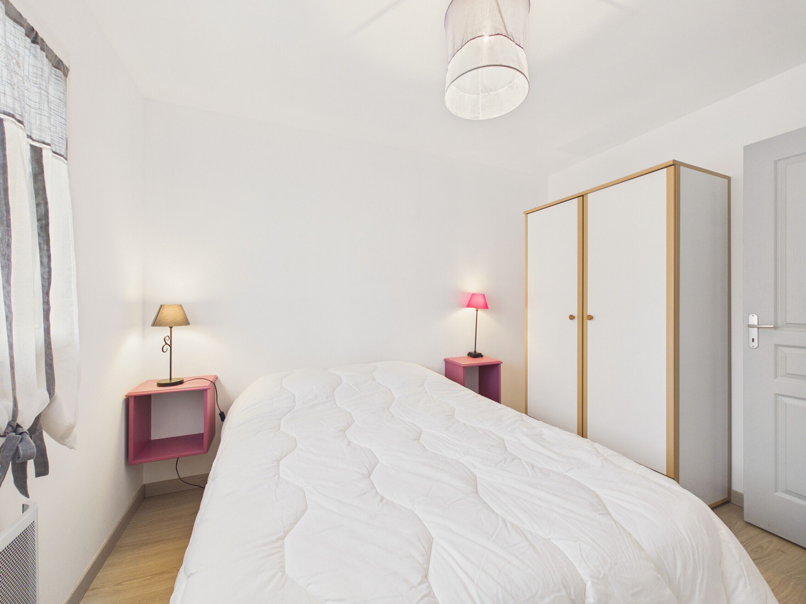 Une chambre à coucher comprenant un lit, deux tables de chevet avec des lampes, une armoire et un luminaire au plafond.