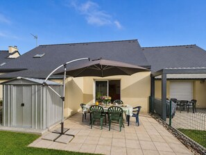 Een terras met tafel en stoelen, een overdekt gedeelte en een omheinde tuin.