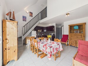 Un coin repas avec une table dressée pour quatre personnes, une cuisine en arrière-plan et un escalier menant à un autre niveau.