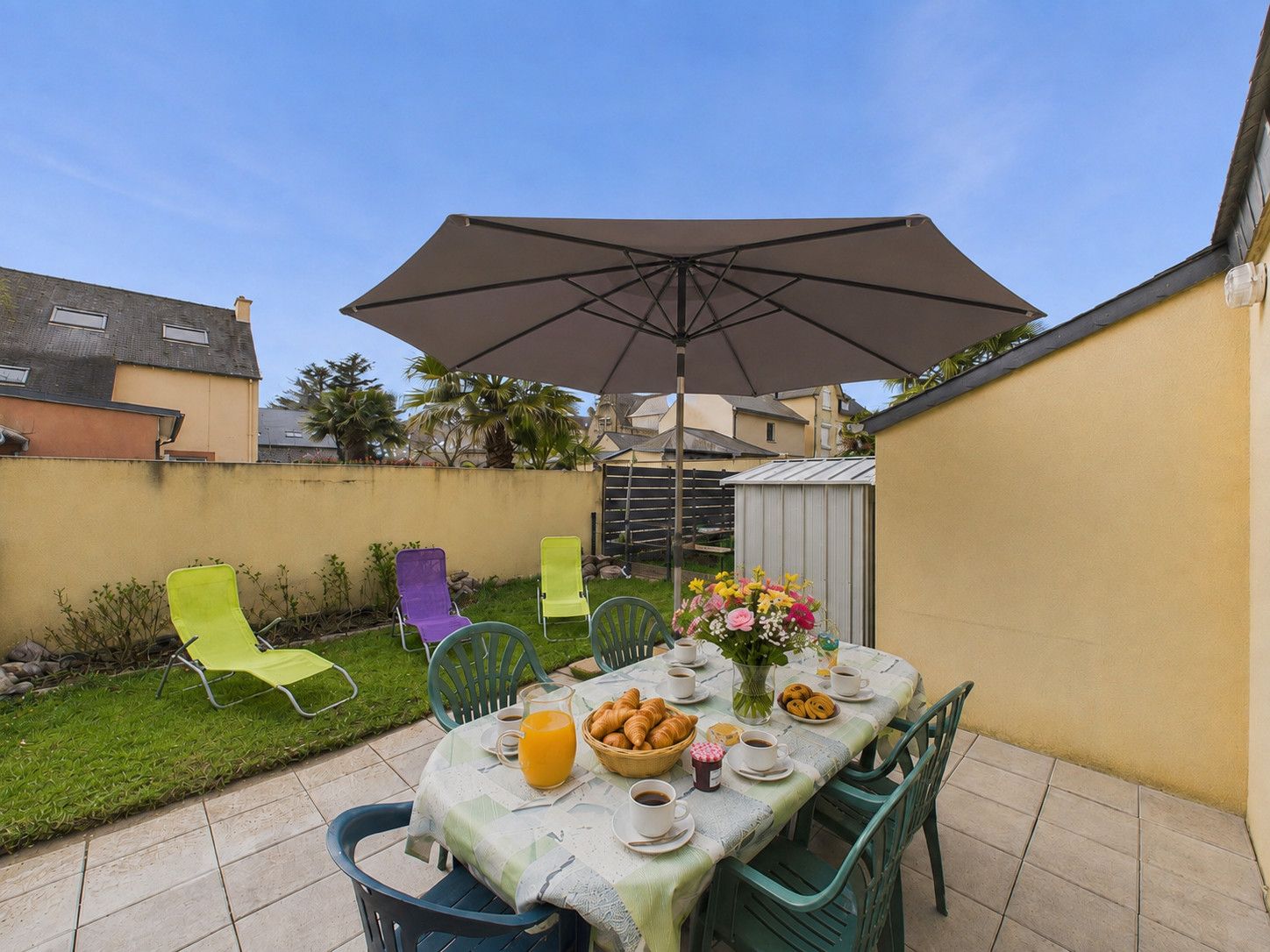 Une terrasse extérieure avec une table dressée pour le petit-déjeuner, comprenant des croissants et du café, sous un grand parasol.