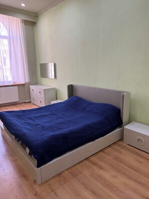 A bedroom with a bed, a dresser, a nightstand, a window with curtains, and a wall-mounted TV. - Rustaveli Avenue City Center Apartment (T'bilisi)