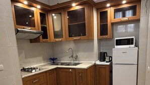 Eine kompakte Küche mit Holzausstattung, einem weißen Kühlschrank, einer Mikrowelle, einem Gasherd und einem Spülbecken.