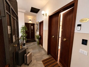 Ein Hotelgang mit Doppeltür, Fußmatte, Wandleuchte, Überwachungskamera und Klingel.