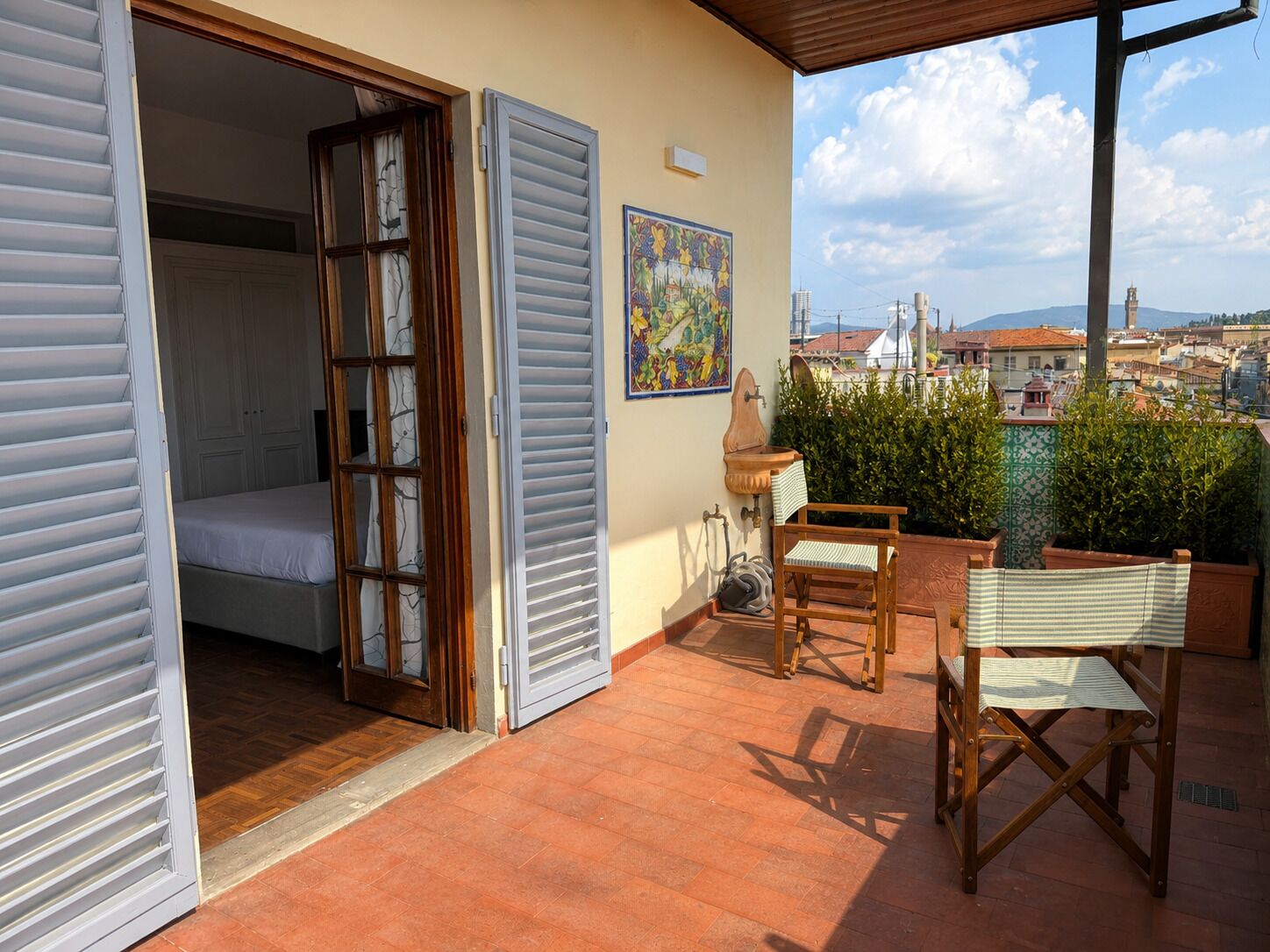 A balcony with a bed, a chair, a sink, and a painting.