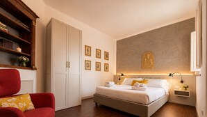 Een hotelkamer met een bed, een rode fauteuil, een kledingkast en een muur met ingelijste foto's.