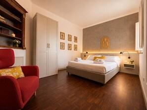 Ein Hotelzimmer mit einem Bett, einem roten Sessel, einem Kleiderschrank und einer Wand mit gerahmten Bildern.