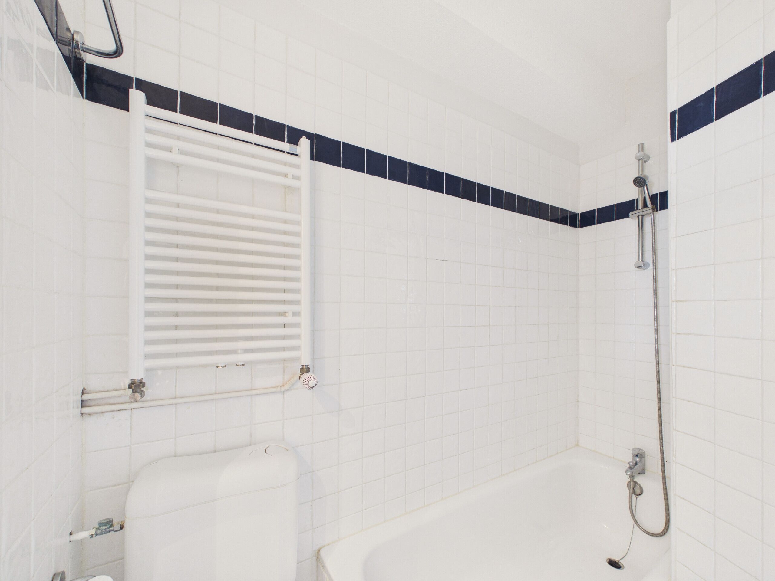 Un bagno con piastrelle bianche, una vasca da bagno, una doccia e un portasciugamani.