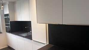 A modern kitchen with white cabinetry, a black countertop, and built-in appliances. - City Apartment in Müllheim (Müllheim im Markgräflerland)