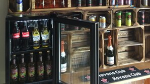 A bar area with shelves of alcoholic beverages, a neon sign, and a display of canned drinks. - City Apartment in Müllheim (Müllheim im Markgräflerland)