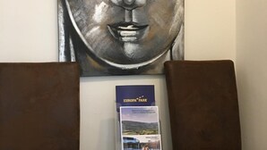 A reception area with a large Buddha statue, two brown upholstered chairs, and a brochure stand. - City Apartment in Müllheim (Müllheim im Markgräflerland)