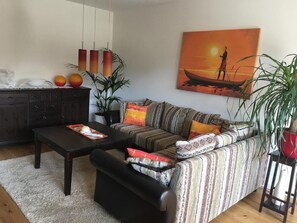 Una sala de estar con un sofá, una mesa de centro, un aparador de madera oscura y un cuadro de un atardecer sobre el agua.
