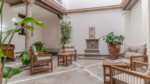 Un vestíbulo amplio con techo alto, una columna central y una zona de estar con muebles de mimbre.