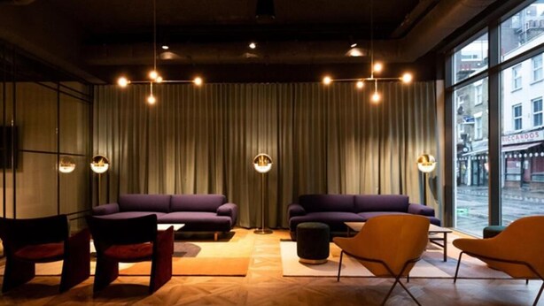 Een moderne zithoek met een groot raam, twee banken, een salontafel en een kleine oranje fauteuil.