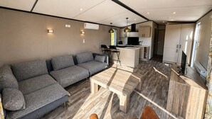 A modern living space with a sofa, a wooden coffee table, and a kitchen area with a TV. - 4-Person Prins Chalet Hoogersmilde (Hoogersmilde)