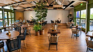 A restaurant with wooden tables and chairs, large windows, and a central plant. - 4-Person Prins Chalet Hoogersmilde (Hoogersmilde)