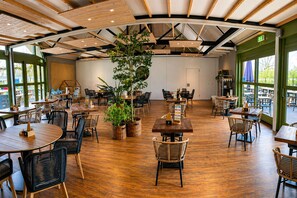 A restaurant with wooden tables and chairs, large windows, and a central plant. - 4-Person Prins Chalet Hoogersmilde (Hoogersmilde)