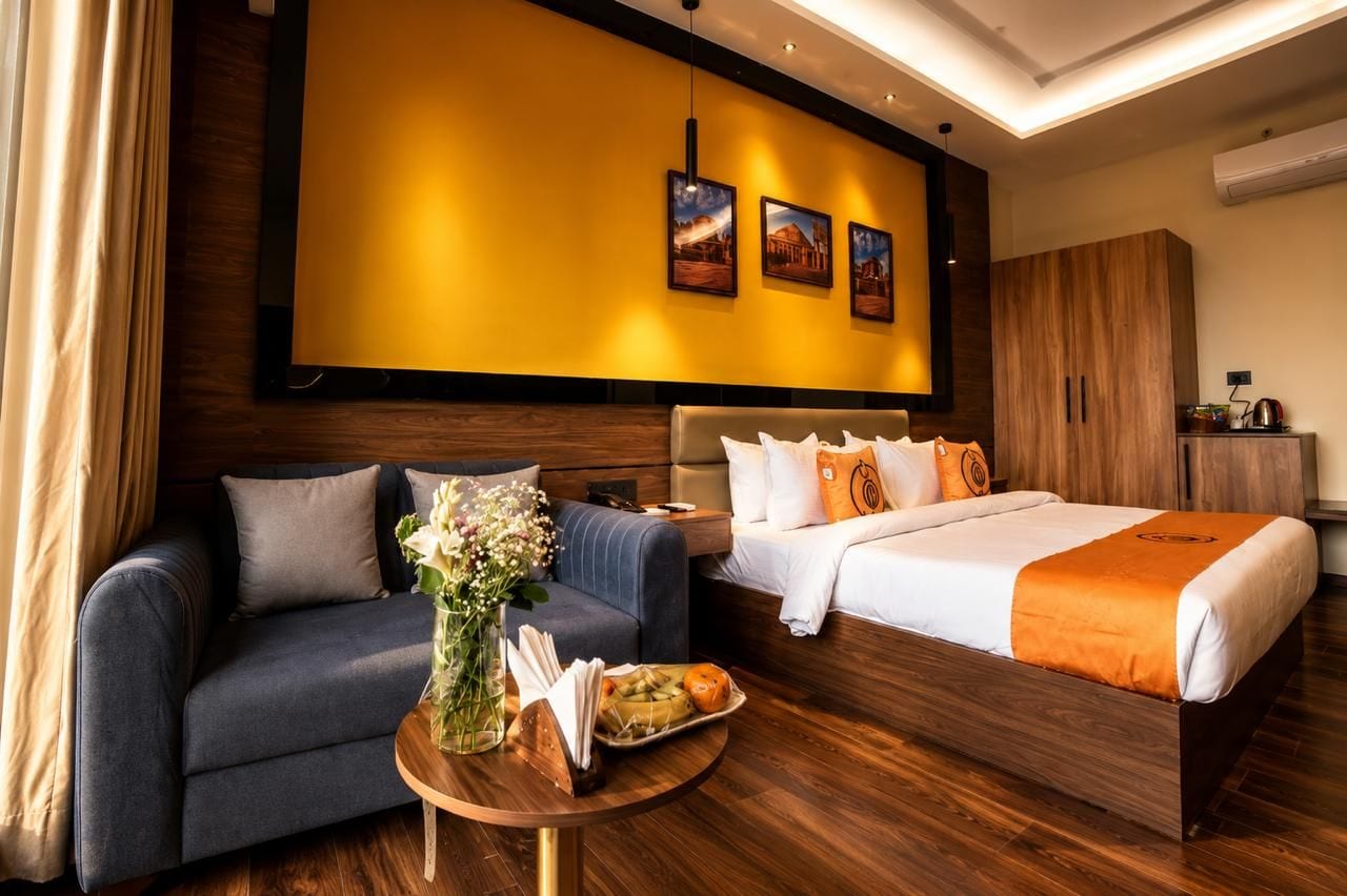 Una habitación de hotel con una cama, un sofá, una mesita con un florero y una bandeja de fruta, además de un armario de madera.