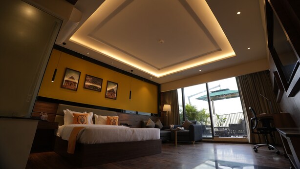 A modern hotel room with a large bed, a sofa, a desk, and a balcony with outdoor seating.
