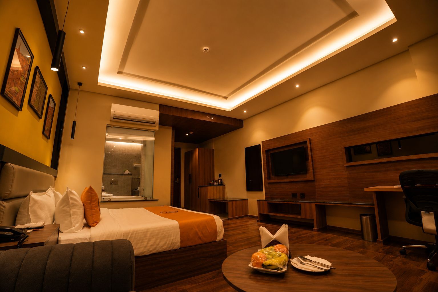 Habitación de hotel moderna con cama, escritorio, televisor y zona de comedor con una mesa lista para dos.