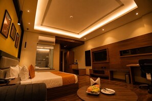 Habitación de hotel moderna con cama, escritorio, televisor y zona de comedor con una mesa lista para dos.