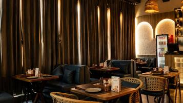 Un interior de restaurante con cortinas oscuras, asientos de cuero, sillas de mimbre y un refrigerador Coca-Cola.