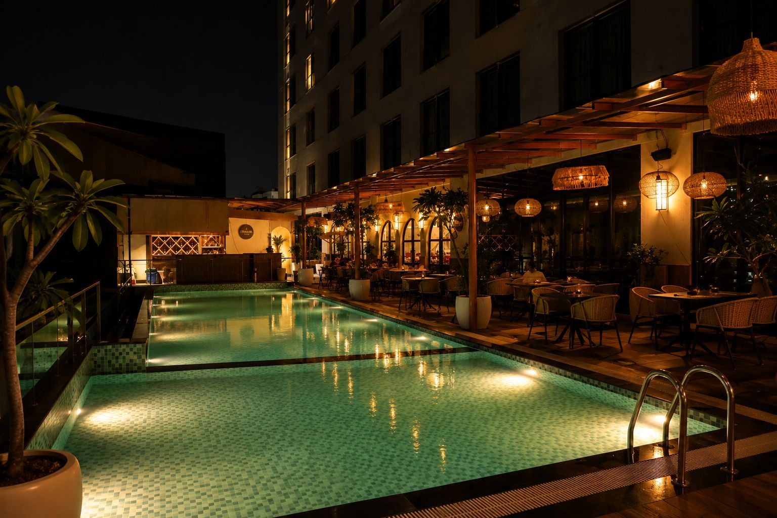 Un área de piscina en la azotea con bar y asientos, rodeada de plantas en macetas e iluminación cálida.