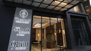 A modern hotel entrance with illuminated signage for The Murti Hotel & Banquet, The Poolwalk Café & Bistro, and Divine Banquets.