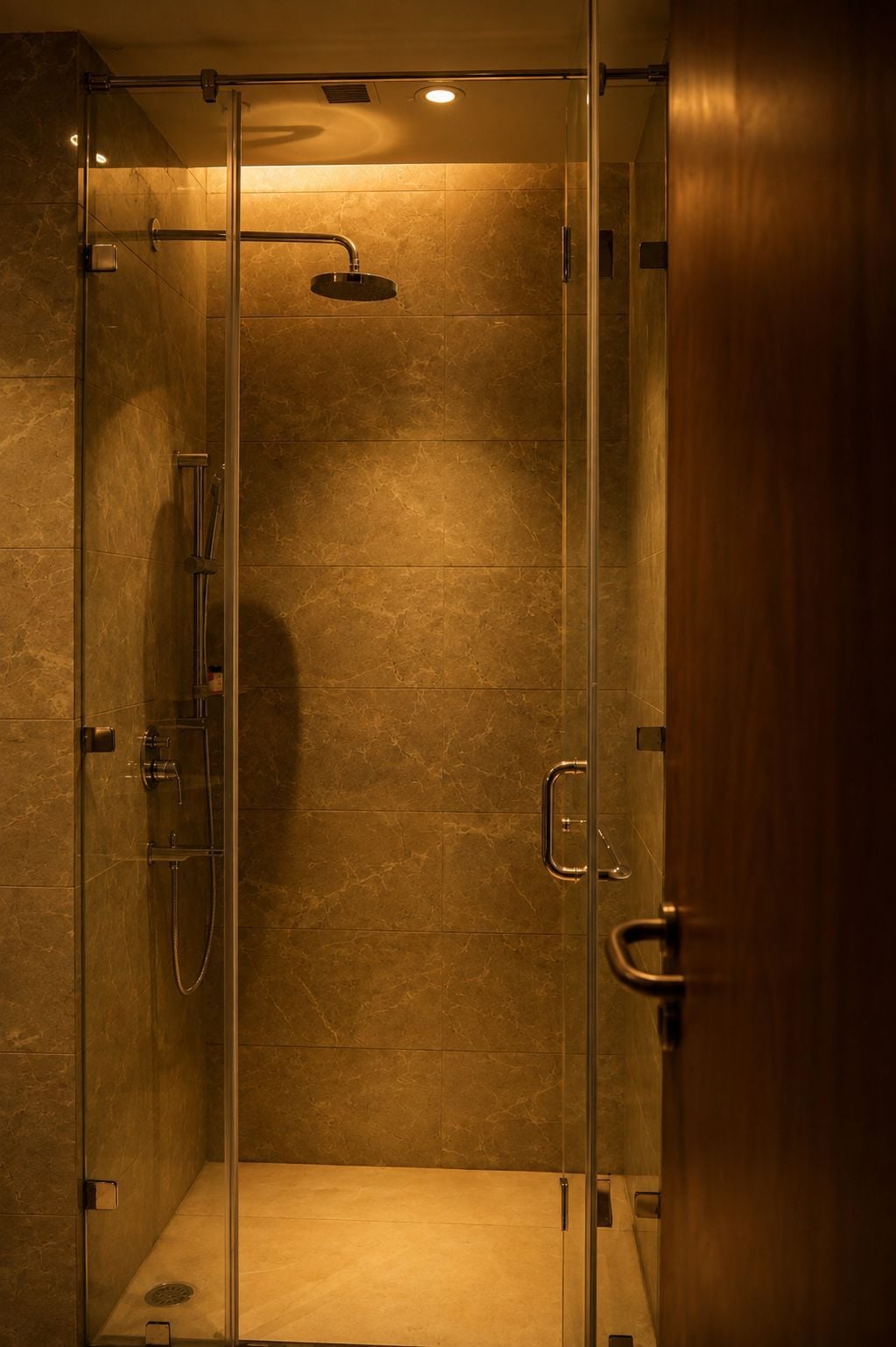 A glass-enclosed shower stall with a handheld showerhead and a handheld faucet.