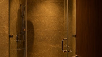 A glass-enclosed shower stall with a handheld showerhead and a handheld faucet.