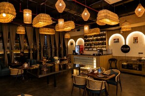 A restaurant interior with hanging wicker chandeliers, a bar area, and a city view through large windows.