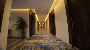 A hotel hallway with a patterned carpet, potted plants, and wooden doors.