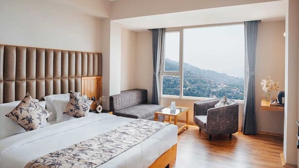 Ein Hotelzimmer mit einem großen Bett, einem Schlafsofa, einem kleinen Tisch und Blick auf eine Stadtlandschaft.