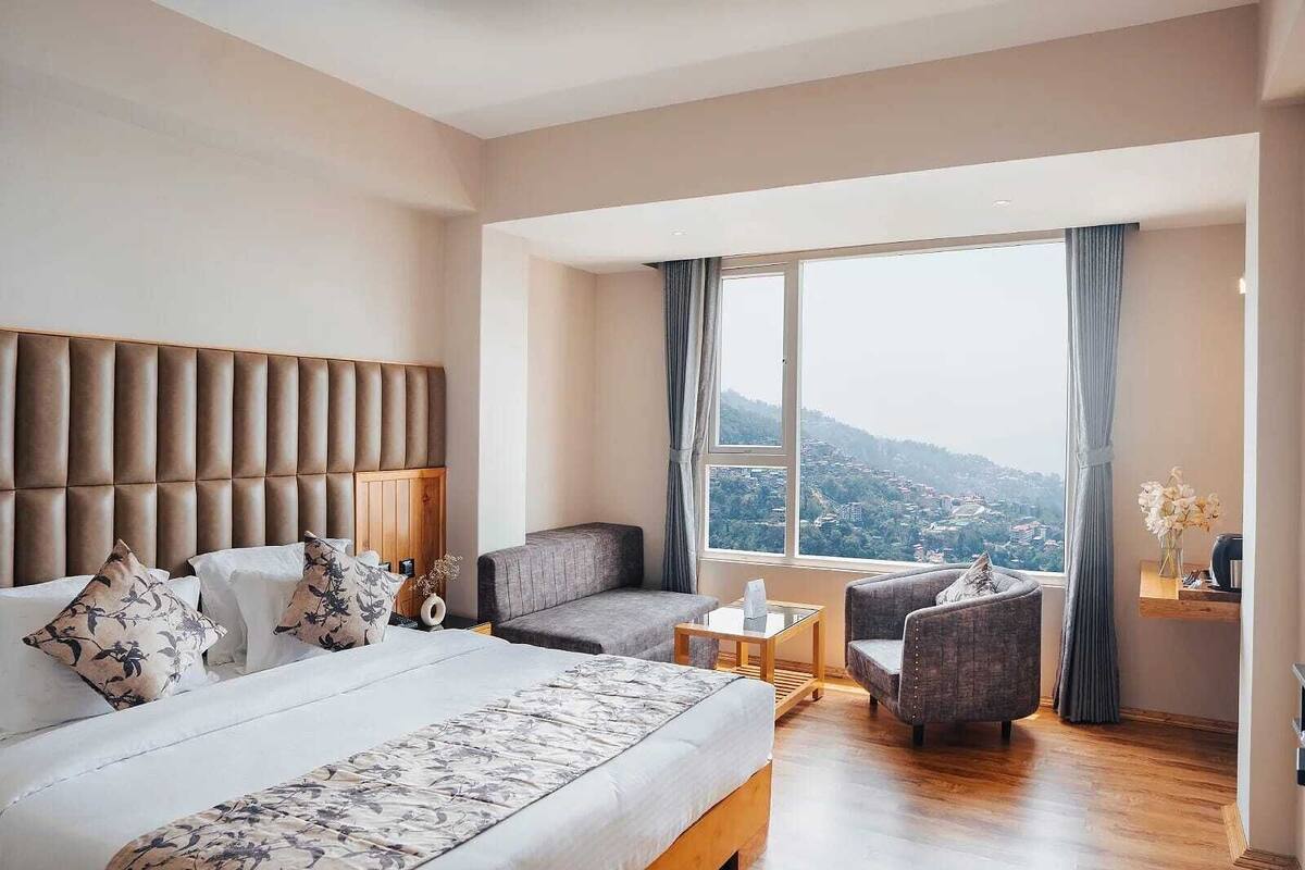 A hotel room with a large bed, a sofa, a small table, and a view of a cityscape.