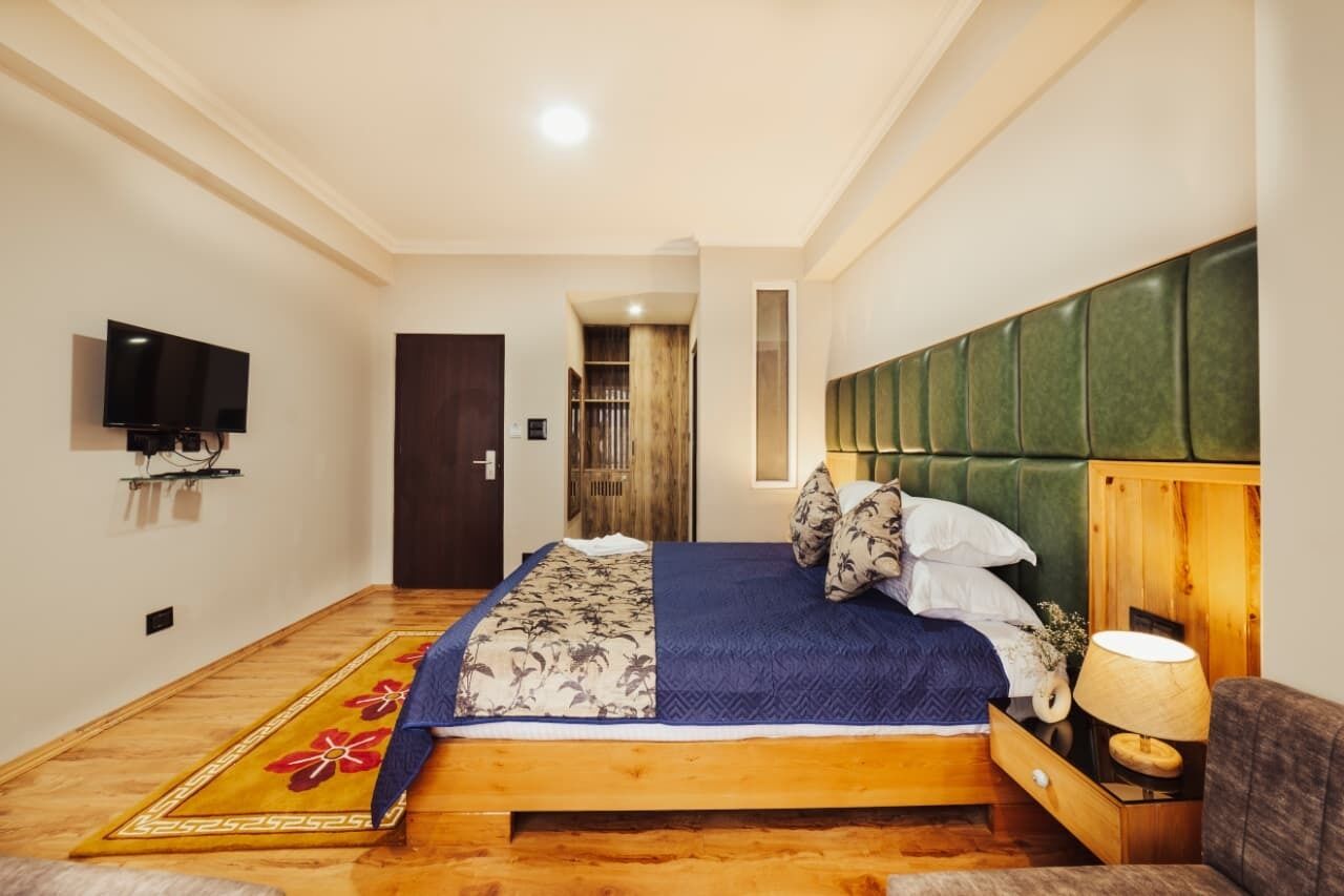A bedroom with a bed, a television, a wooden headboard, a nightstand, and a lamp.