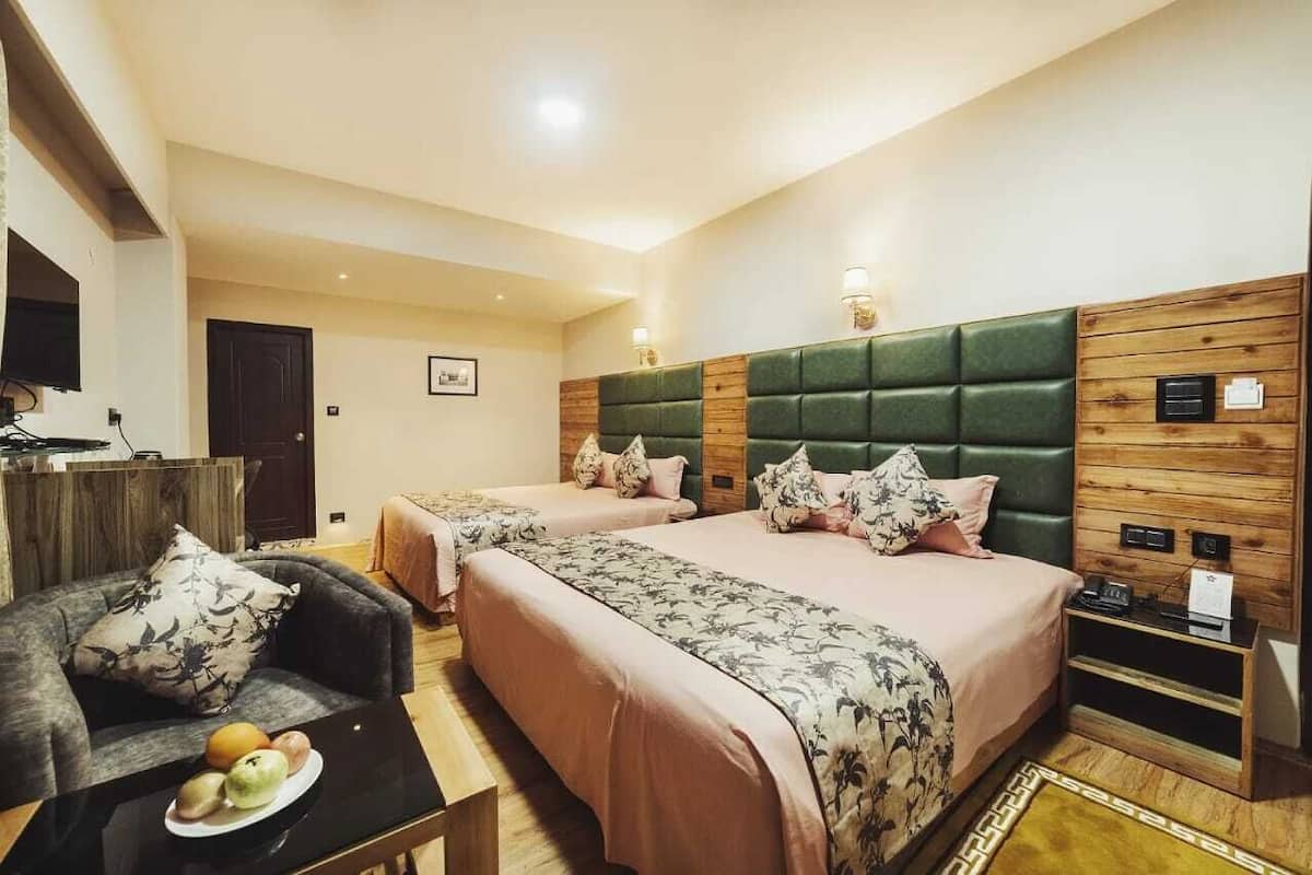A hotel room with two beds, a sofa, a small table with fruit, and a TV.