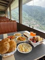 A dining table with food, drinks, and a view of a mountainous landscape.
