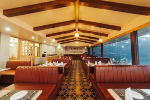 A restaurant with booths and tables, wooden beams on the ceiling, and a view of the city.