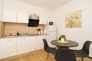 A modern kitchen with white cabinets, a microwave, and a dining area with a round table and black chairs. - Elegant apartment for 2 with sea view (Dramalj)