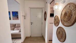 A hallway with a white door, beige tiles, a sofa, and wall-mounted woven baskets. - Sweet Escape apartment on the beachfront (Orpesa)