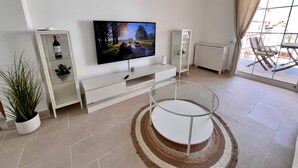 A modern living room with a flat-screen TV, a white entertainment unit, a glass coffee table, and a view through a large window. - Sweet Escape apartment on the beachfront (Orpesa)