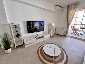A modern living room with a flat-screen TV, a white entertainment unit, a glass coffee table, and a view through a large window. - Sweet Escape apartment on the beachfront (Orpesa)