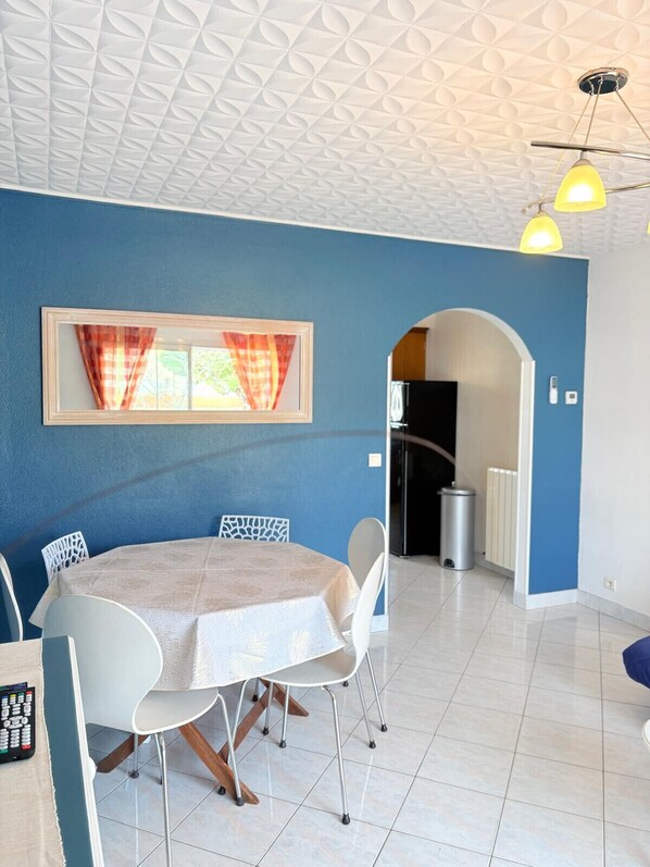 A dining area with a table and chairs, a window with curtains, a radiator, and a door leading to another room. - St Cyprien Cocon: Beach, market and shops within walking distance (Saint-Cyprien)