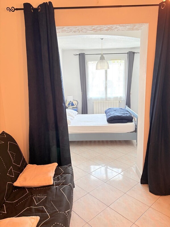 A bedroom with a bed, a window with curtains, a radiator, and a hanging light fixture. - St Cyprien Cocon: Beach, market and shops within walking distance (Saint-Cyprien)