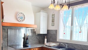 Uma cozinha com armários de madeira, uma mesa redonda com toalha de mesa azul, um relógio e luminárias pendentes.