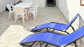 Um edifício de dois andares com um pátio, que inclui uma mesa e cadeiras, uma área de estar coberta e uma porta de acesso ao interior.