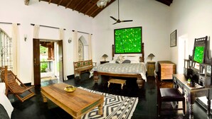 Una habitación con una cama, una mesa de madera, un escritorio, una silla, un ventilador de techo y un tapiz grande de color verde con motivos.