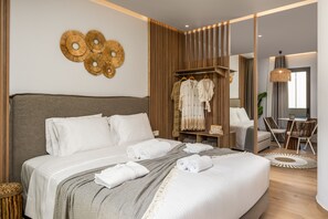A modern hotel room with a large bed, a wardrobe, a seating area, and a dining table. - Oasis Luxury Suites (Rhodes)
