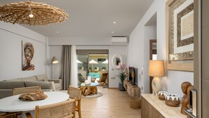 A modern living room with a round dining table, wicker chairs, a sofa, a large mirror, and a ceiling light fixture.